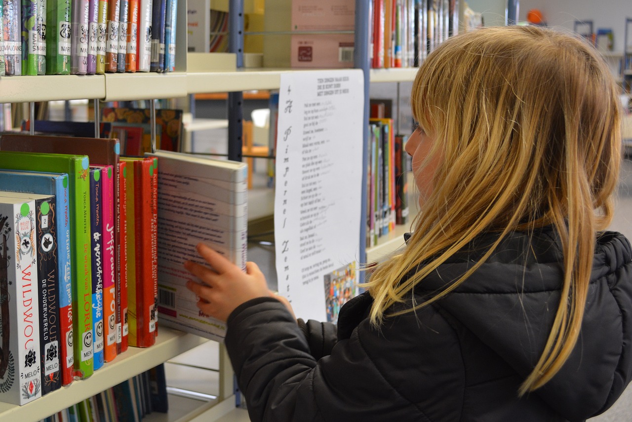 Lapsi ojentaa kätensä kohti kirjaston kirjahyllyn kirjaa.